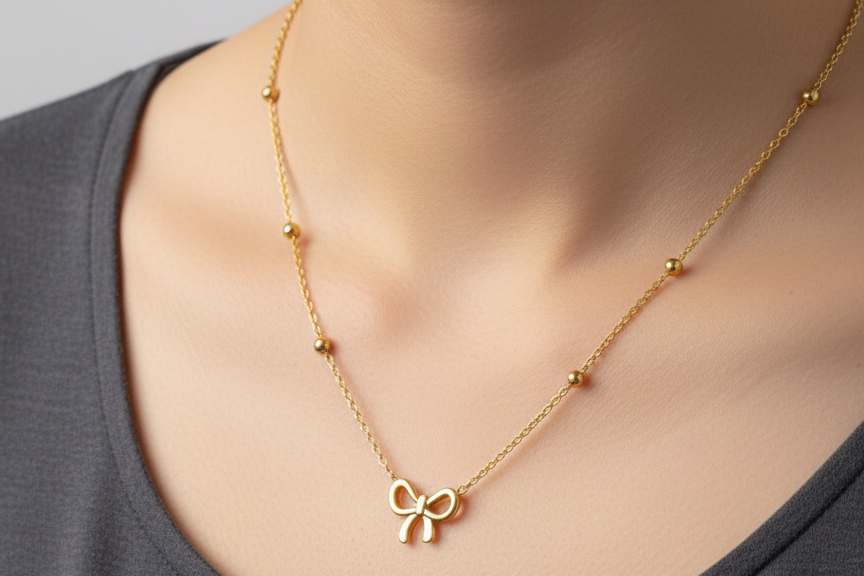 Gold necklace with a bow pendant on a person wearing a gray top.