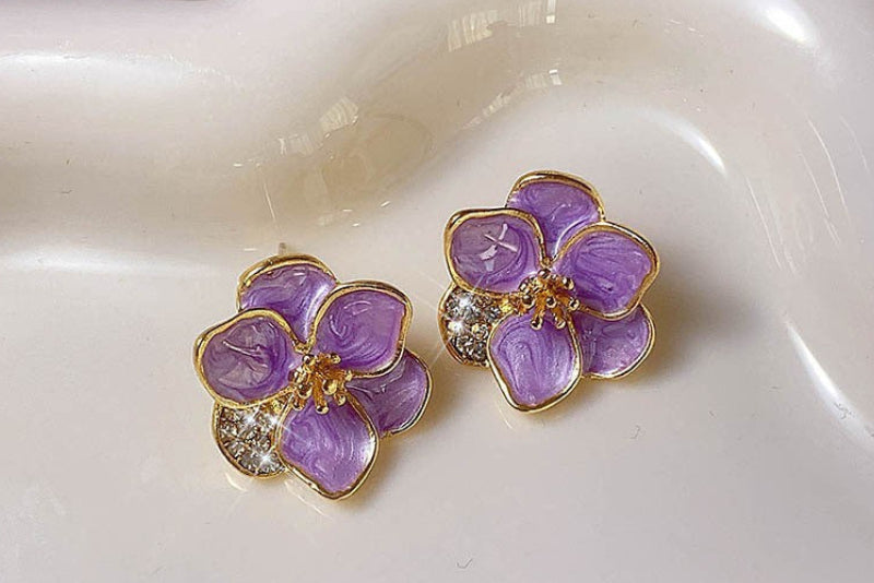 Purple flower-shaped earrings with gold accents on a white dish.