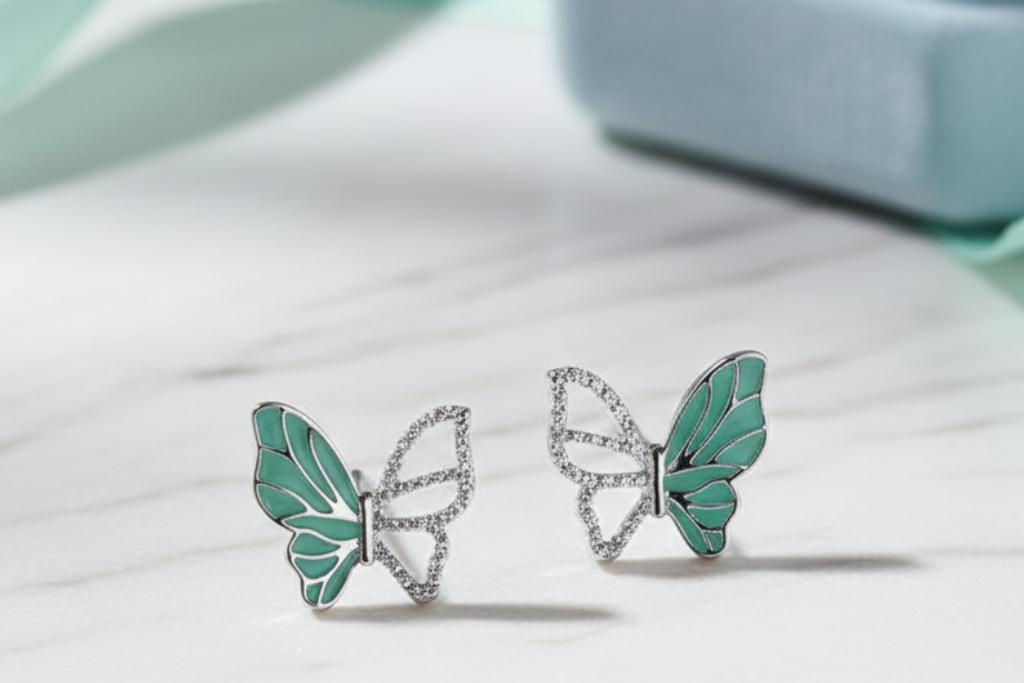 Butterfly-shaped earrings with green wings and silver bodies on a light background