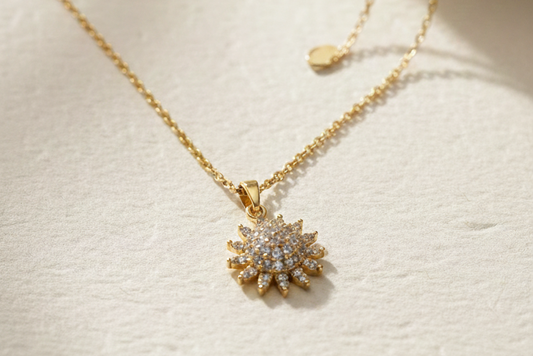 Gold necklace with a sunflower pendant on a light surface