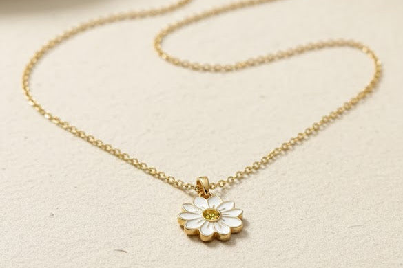 Gold necklace with a daisy pendant on a beige surface