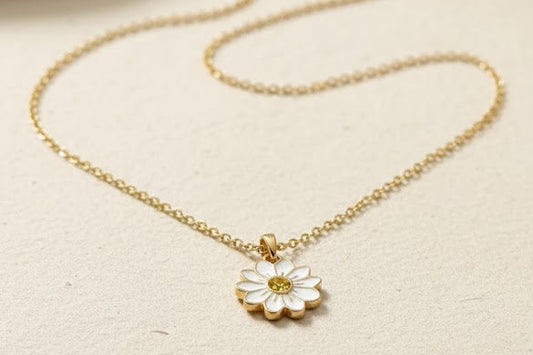 Gold necklace with a daisy pendant on a beige surface